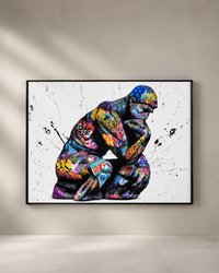 A framed wall art print showing a colorful, graffiti-style depiction of a crouching human figure on a white background, hung on a beige wall above a light floor.