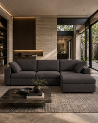 A modern dark gray sectional sofa with a chaise lounge, styled in a contemporary minimalist living room with a marble coffee table and textured rug.