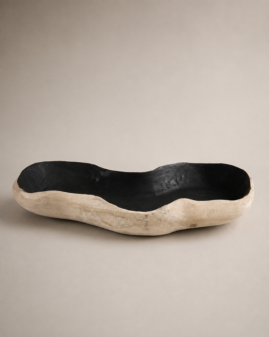 A rustic, organic-shaped wooden bowl with a black lacquered interior and a natural light beige wood exterior, photographed on a neutral beige background.