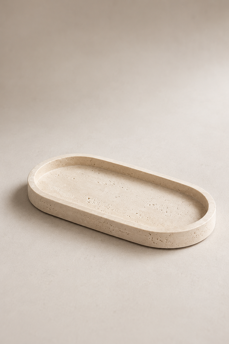 An oval concrete tray with a textured, speckled beige surface, photographed on a matching neutral beige background.