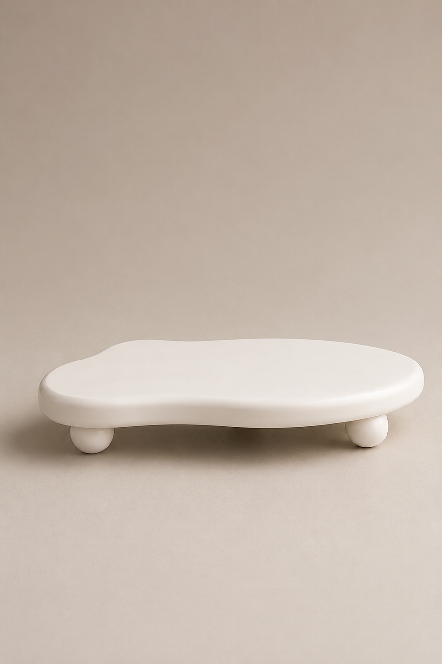 A minimalist, organic-shaped white ceramic shelf or stool with small round feet, set against a solid warm beige background.