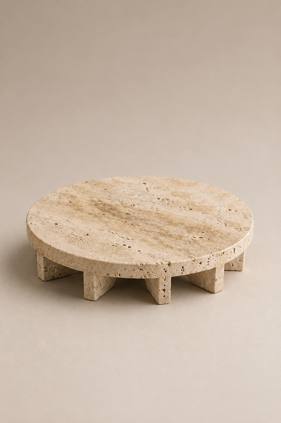 A round travertine stone coffee table with a textured natural stone top and four short block legs, shown on a neutral beige background.