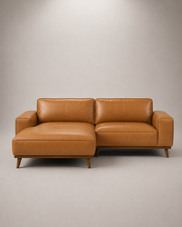 A mid-century modern two-seater sofa with a left-facing chaise lounge, upholstered in warm camel brown leather with tapered wooden legs, set against a neutral gray studio background.