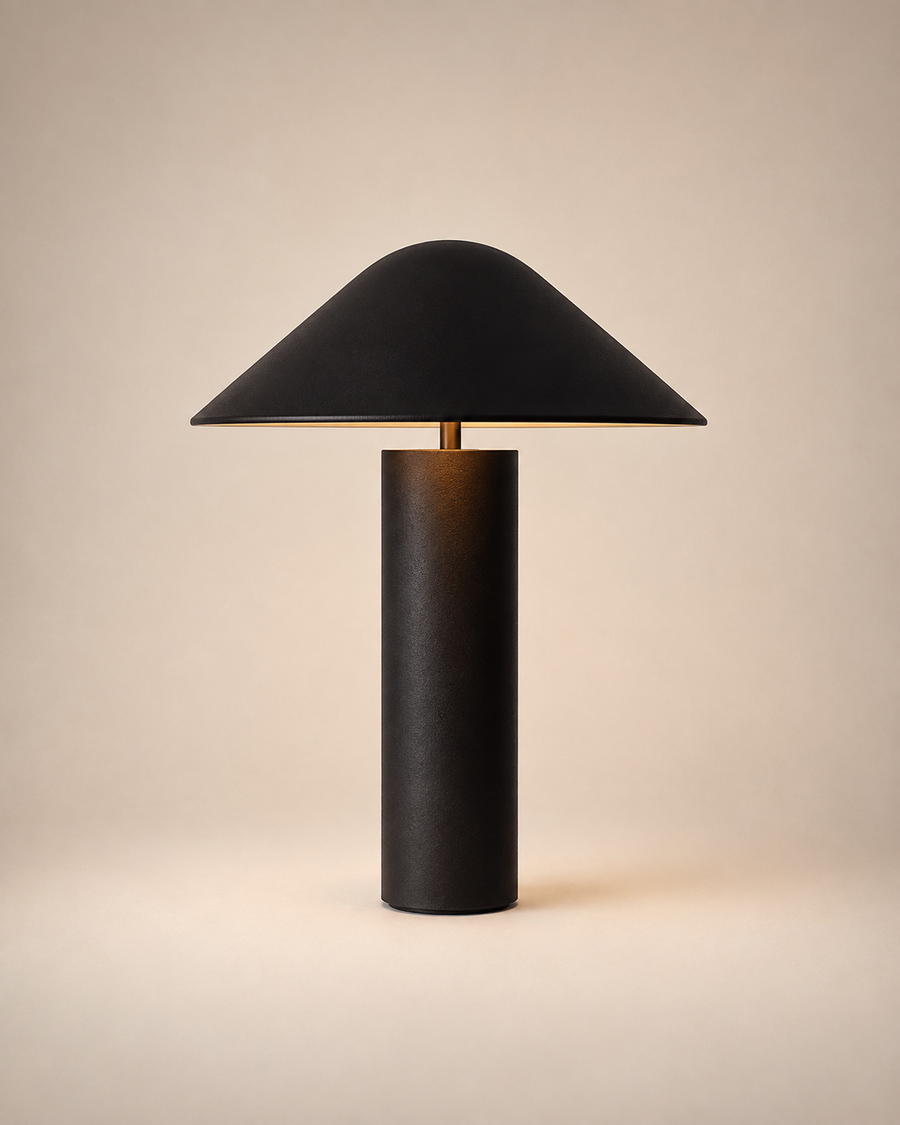 A modern table lamp with a matte black conical shade and a cylindrical black base, illuminated with a warm glow from within, set against a solid beige background.