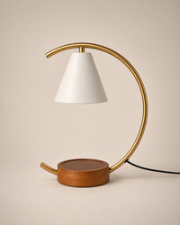 A modern table lamp with a white conical shade, a curved brass metal frame, and a round wooden base, shown on a warm beige background.
