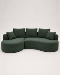 A curved modular upholstered sofa in dark green corduroy fabric with matching square throw pillows, photographed against a plain light gray studio background.