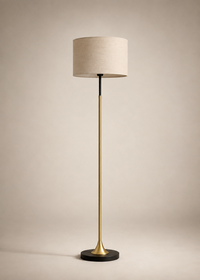 A modern floor lamp with a beige fabric drum shade, a brushed brass gold stem, and a black circular base, set against a warm beige studio background.