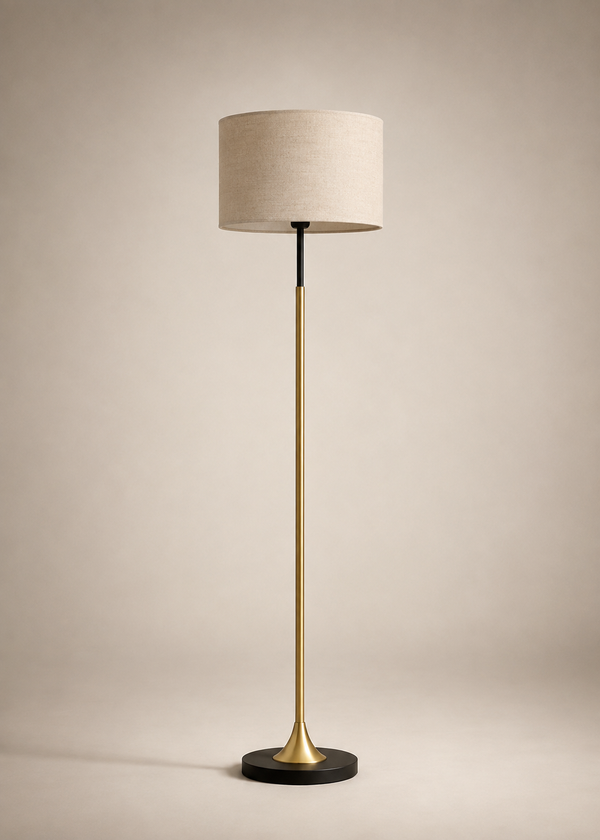 A modern floor lamp with a beige fabric drum shade, a brushed brass gold stem, and a black circular base, set against a warm beige studio background.