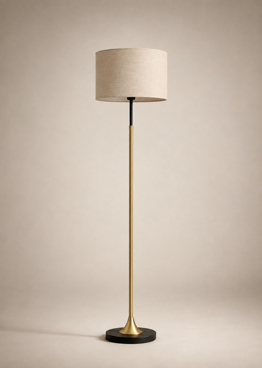 A modern floor lamp with a beige fabric drum shade, a brushed brass gold stem, and a black circular base, set against a warm beige studio background.