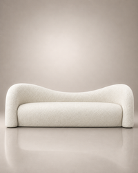 A modern curved sofa upholstered in a textured cream bouclé fabric, set against a minimalist beige studio background with a soft reflection on the floor.