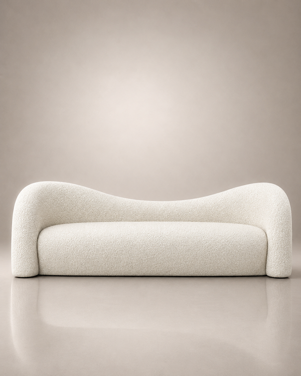 A modern curved sofa upholstered in a textured cream bouclé fabric, set against a minimalist beige studio background with a soft reflection on the floor.
