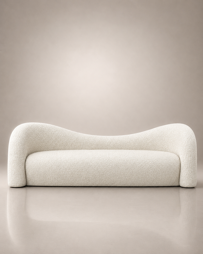A modern curved sofa upholstered in a textured cream bouclé fabric, set against a minimalist beige studio background with a soft reflection on the floor.