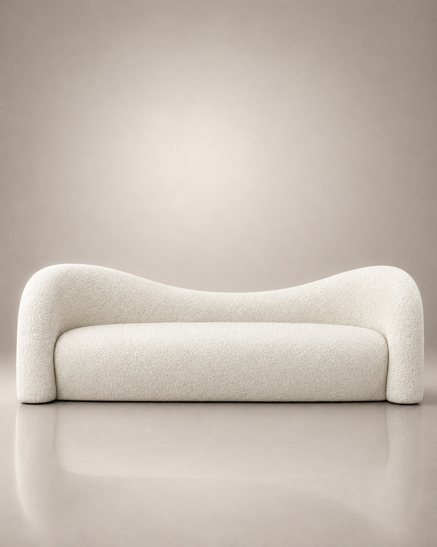 A modern curved sofa upholstered in a textured cream bouclé fabric, set against a minimalist beige studio background with a soft reflection on the floor.