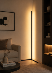 A modern slim floor lamp with a black frame and warm glowing light, positioned in a minimalist living room corner next to a beige sofa and dark wood shelving.