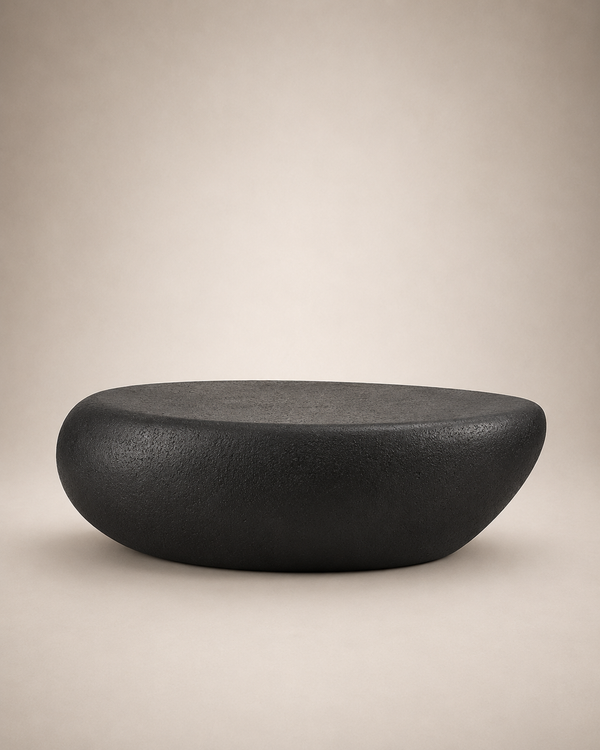 A modern, minimalist oval-shaped black stone or concrete stool with a textured matte finish, set against a warm beige gradient background.