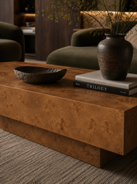 A modern rectangular coffee table with a rich, textured brown burl wood grain finish, styled in a cozy living room setting with a dark bowl, books, and a ceramic vase.