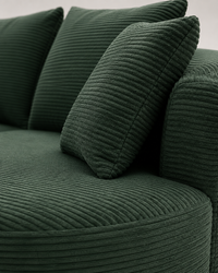 Close-up of a dark green corduroy sofa with matching throw pillows, showing the ribbed fabric texture and curved arm details.