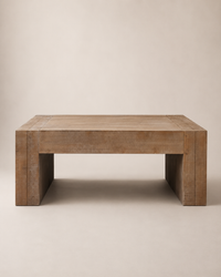 A rustic rectangular wooden coffee table with thick blocky legs, shown from a front angle against a solid beige background.