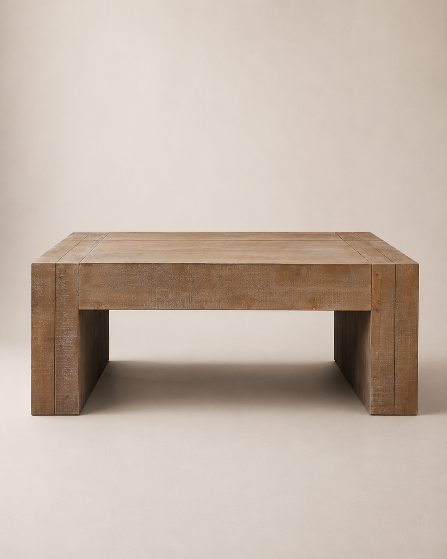 A rustic rectangular wooden coffee table with thick blocky legs, shown from a front angle against a solid beige background.
