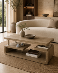 A modern wooden coffee table with a two-tier design, styled in a warm, contemporary living room next to a curved cream sofa.