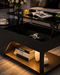 A modern black lift-top coffee table with gold interior shelving, styled in a living room setting with books, a vase, and an open magazine on the tabletop.