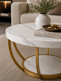 A round coffee table with a white marble-patterned top and base, supported by a gold metal frame, styled in a modern living room setting.