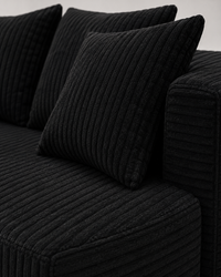 Close-up of a black ribbed corduroy sofa with matching black throw pillows, showing the textured fabric detail.