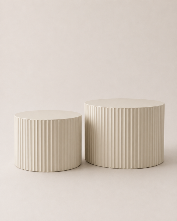 Two ribbed cylindrical side tables in a warm off-white or cream color, shown on a seamless light beige studio background.